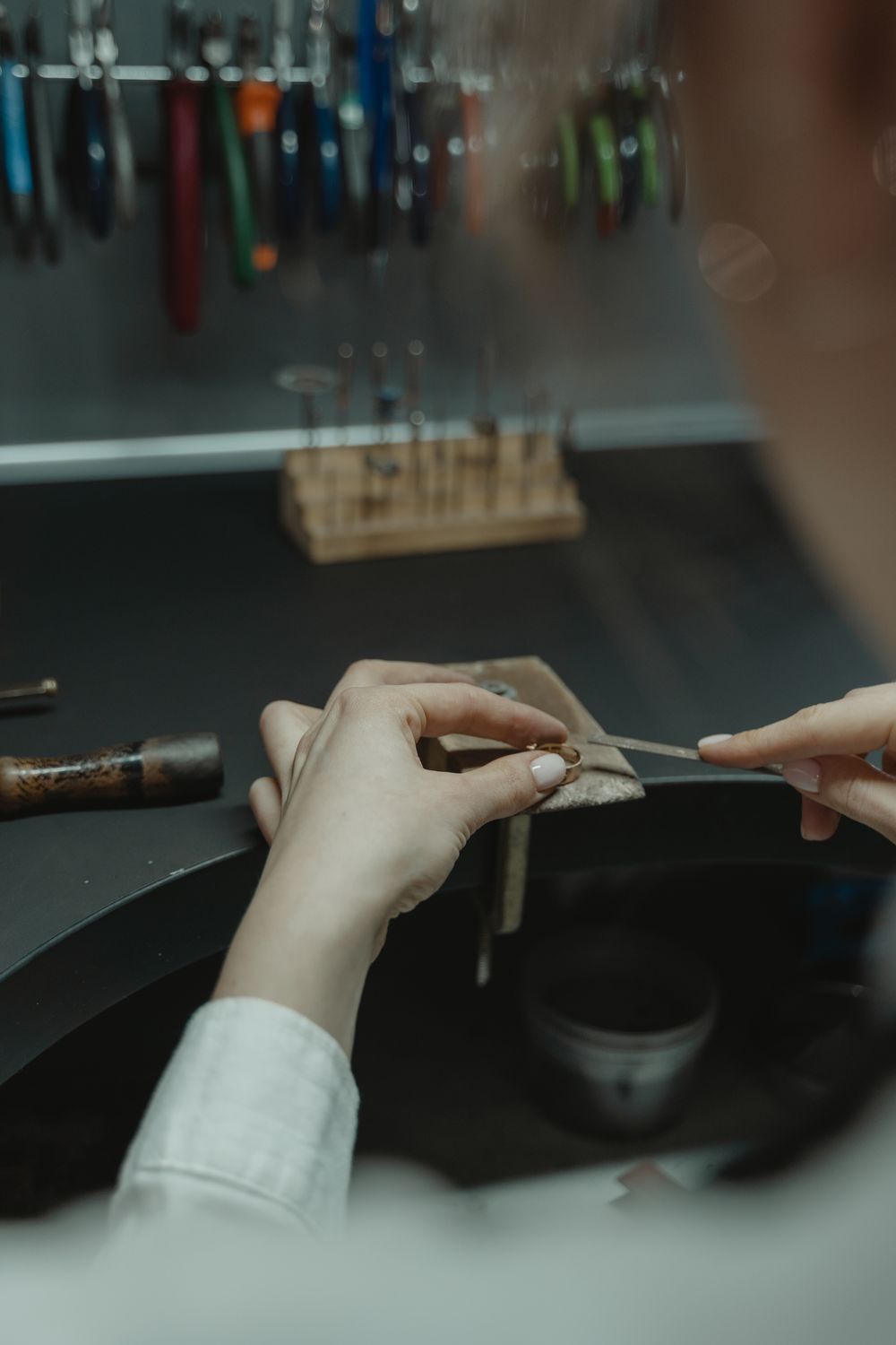 Hands filing a ring held against the bench peg in a jeweller's workshop
