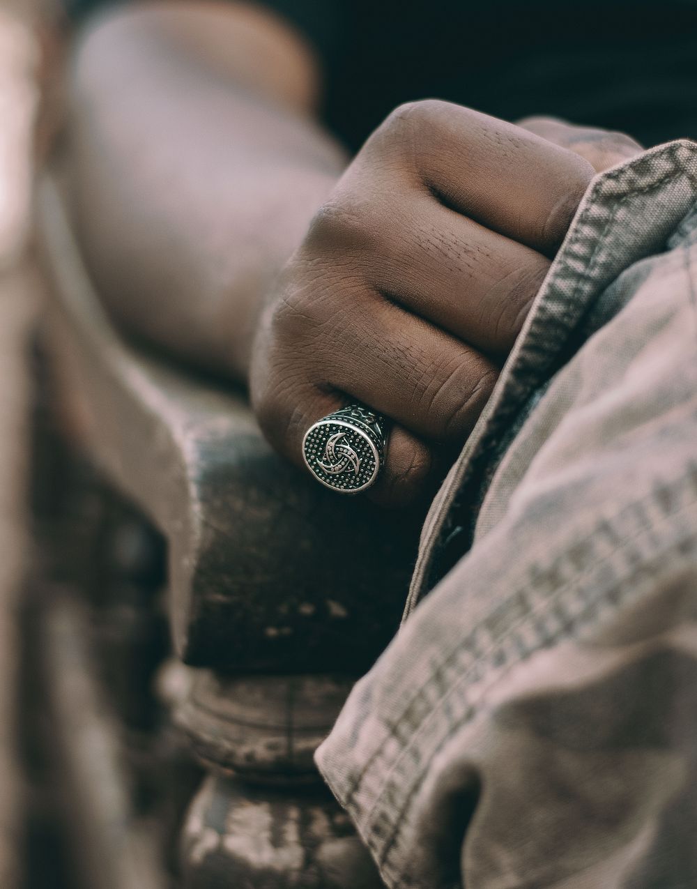 A silver oval signet ring on a man's hand resting on a wooden chair arm