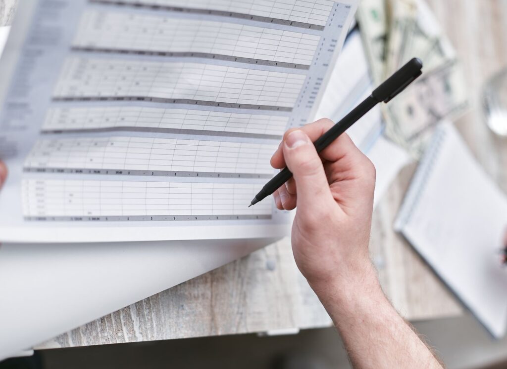 A person with a pen checking a column of figures on a document