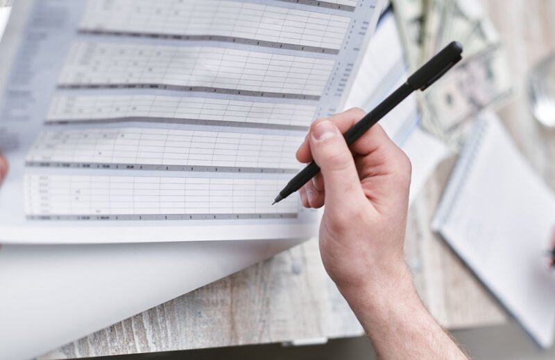 A person with a pen checking a column of figures on a document
