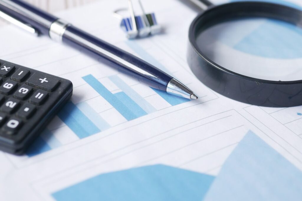 A calculator, a pen and a magnifying glass on printed financial documents