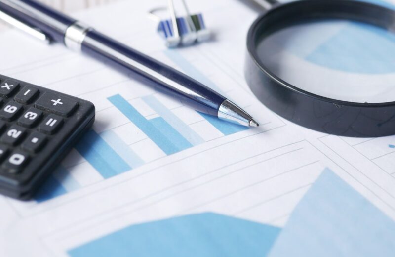 A calculator, a pen and a magnifying glass on printed financial documents