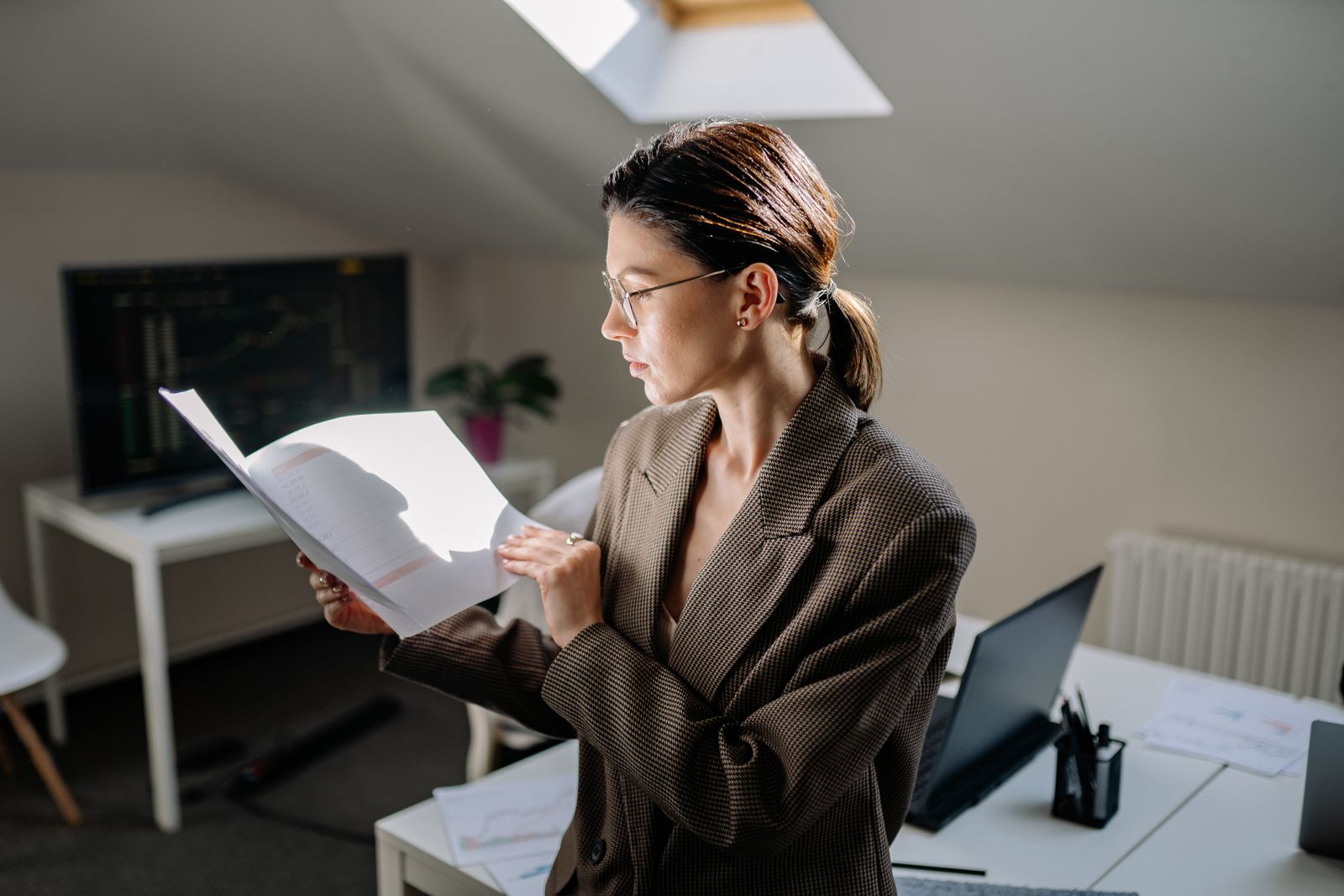 A portfolio manager in glasses reading a printed report at her desk