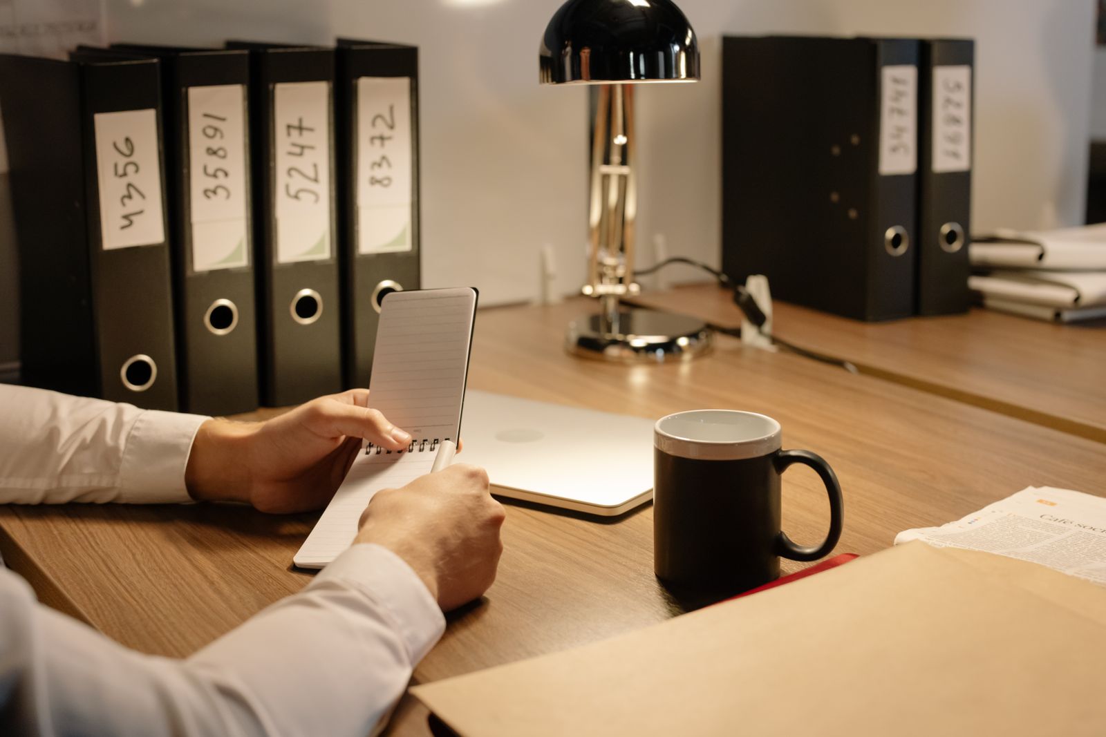 A person reading notes at a desk in front of numbered binders on a shelf
