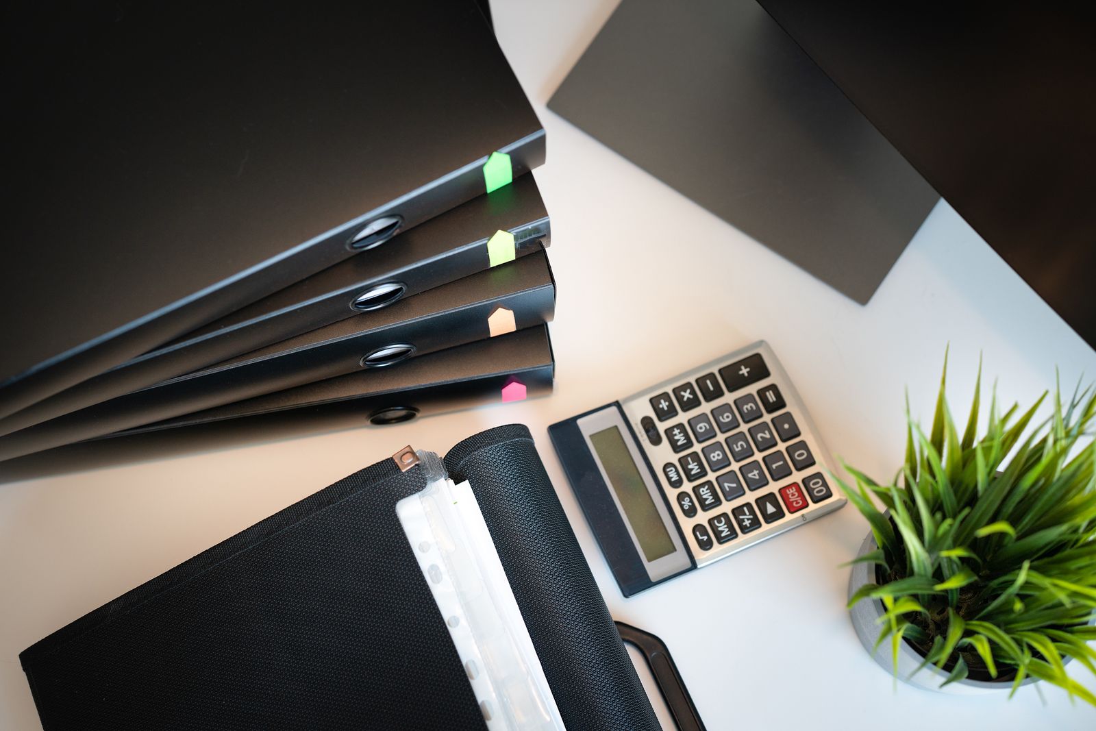 A tidy office desk from above with files, a calculator and a small plant