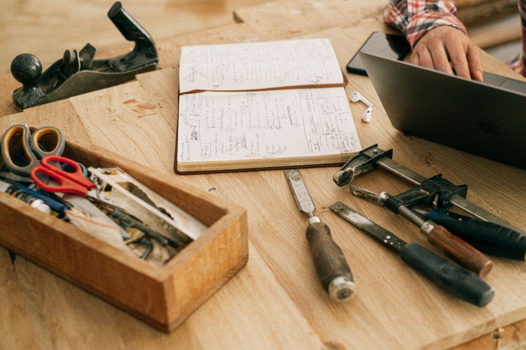 Woodworking tools, a notebook and a laptop on a workshop bench