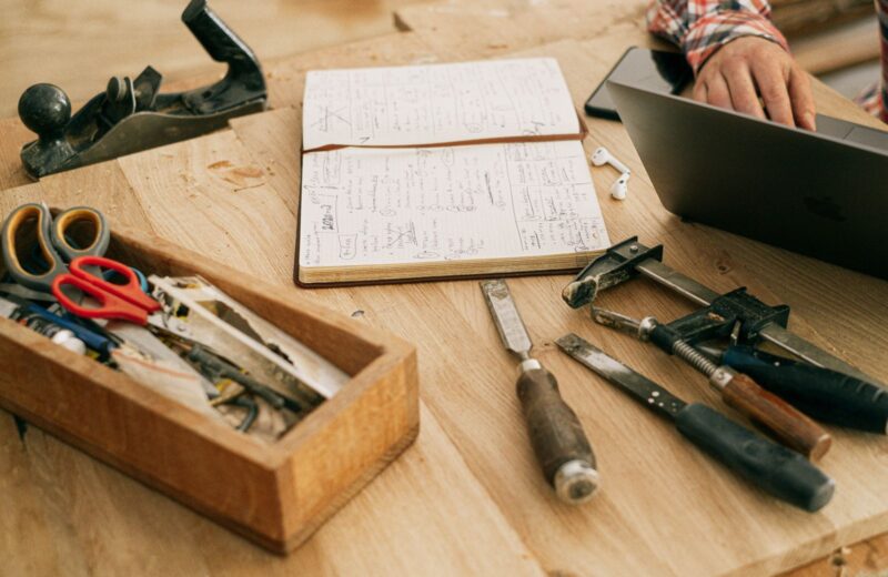 Woodworking tools, a notebook and a laptop on a workshop bench