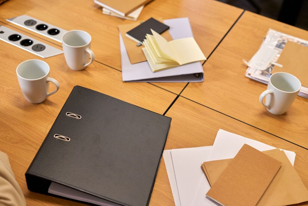 A desk with binders, papers and coffee mugs