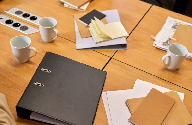 A desk with binders, papers and coffee mugs