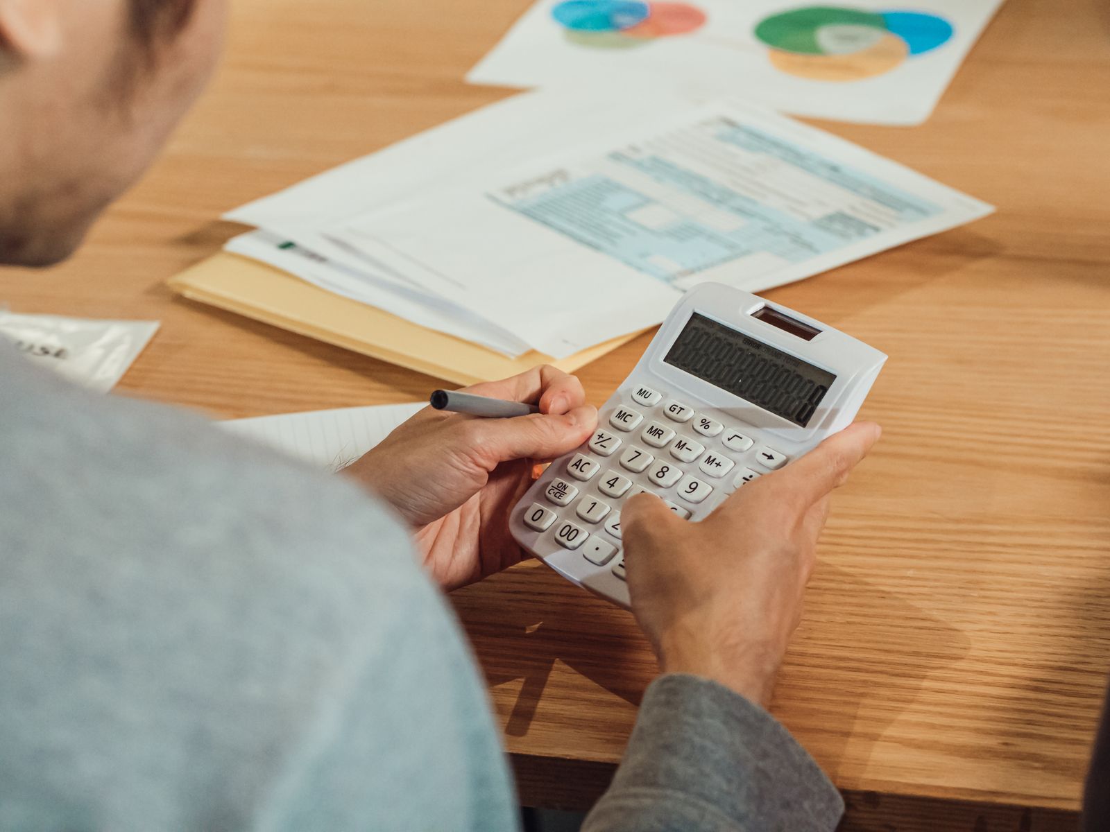 Hands using a calculator over printed statements on a wooden desk
