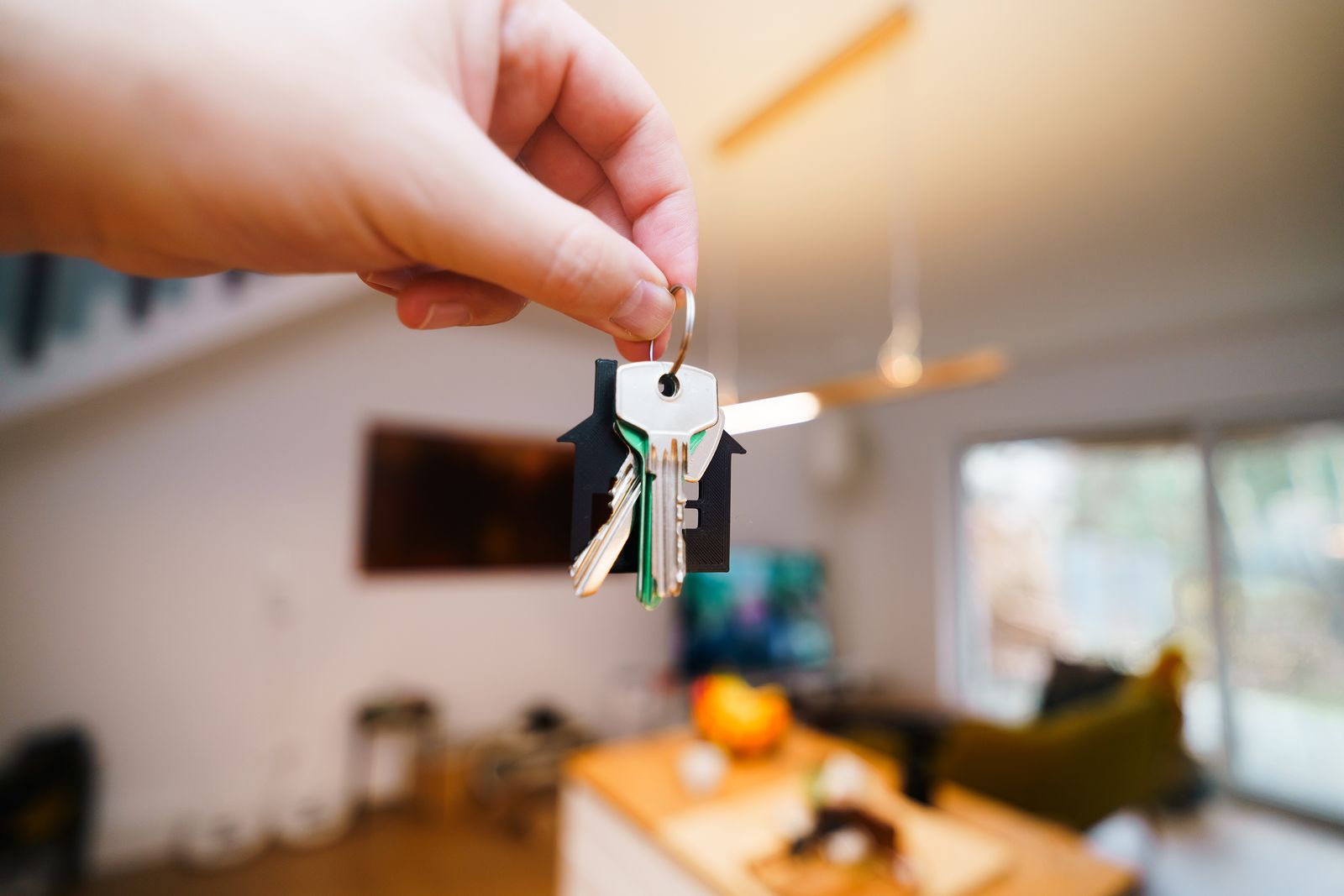 A hand holding a set of house keys in a bright living room