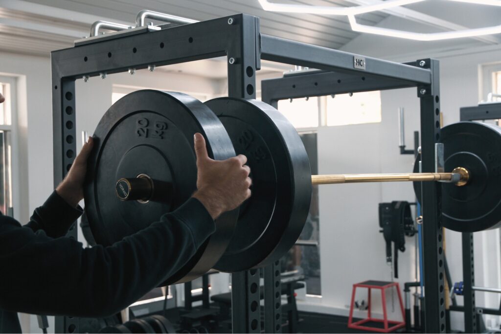 A lifter slides a bumper plate onto a barbell in the rack