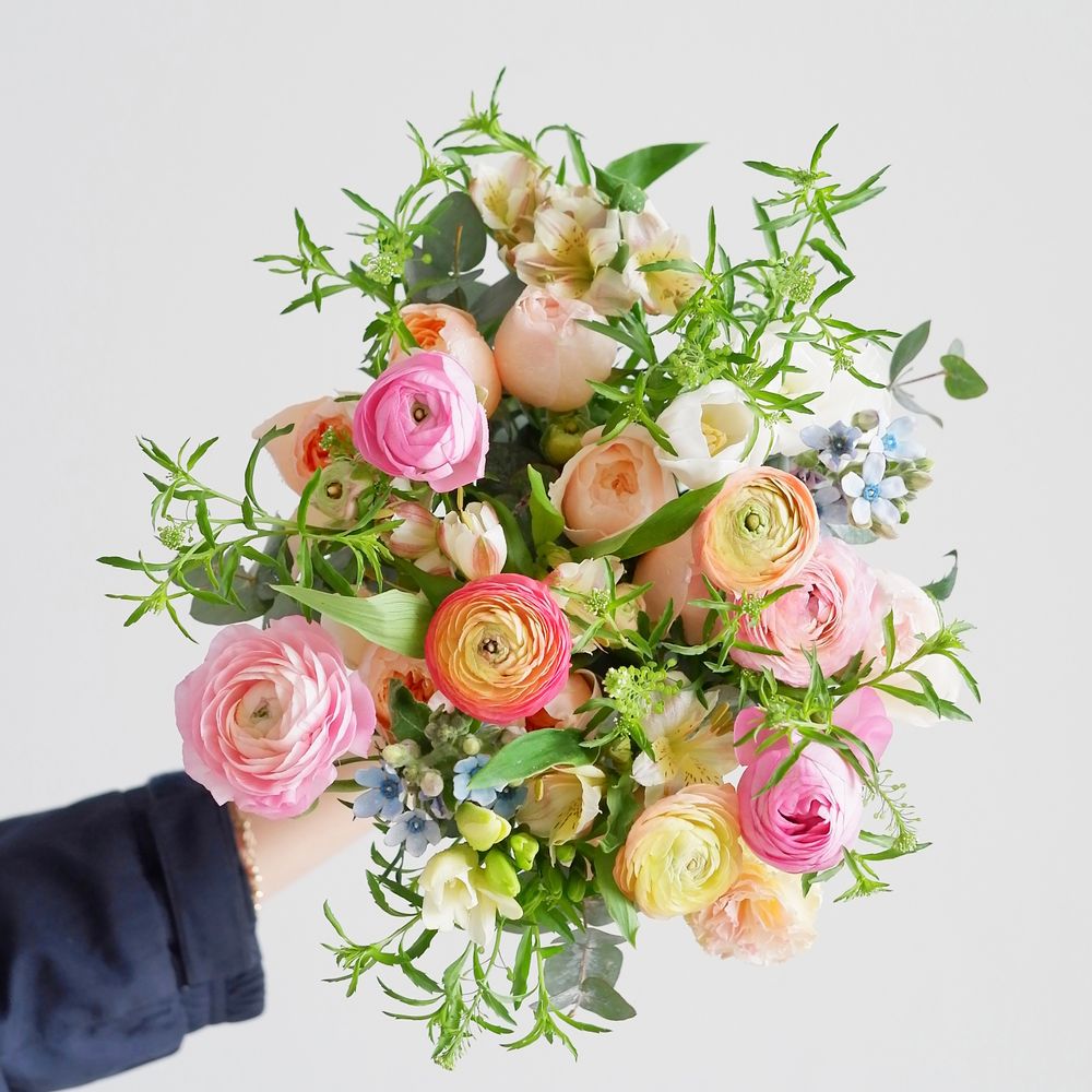 A colourful hand-tied bouquet of roses and garden flowers held against a white wall