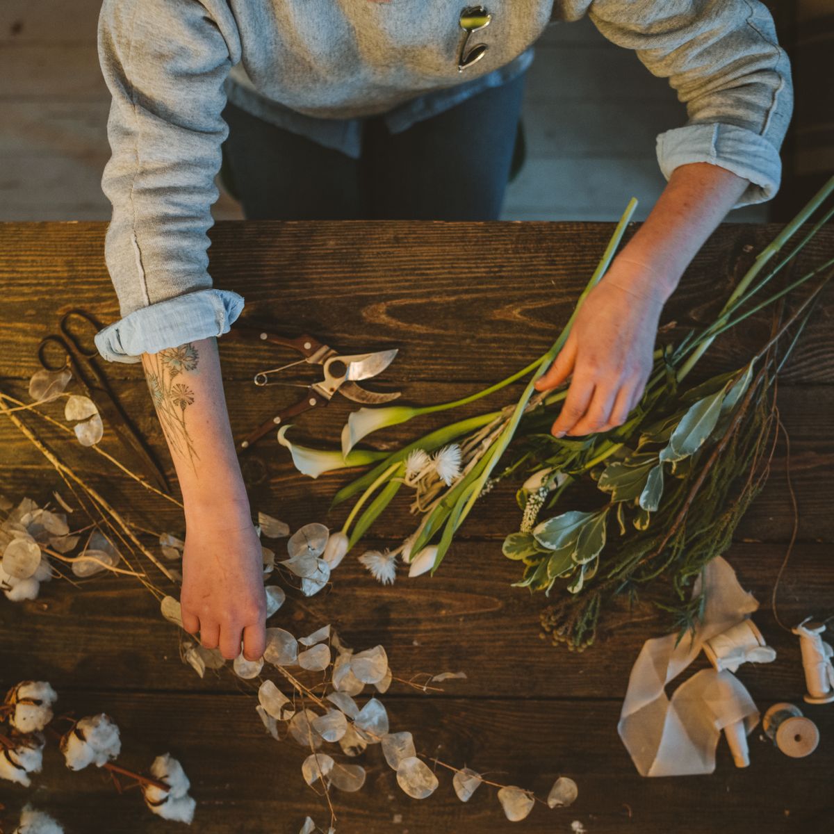 A florist's hands sorting stems and leaves on a wooden bench