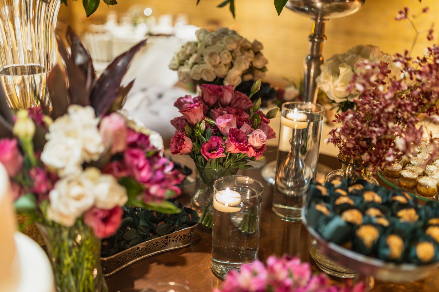 An evening table with flower arrangements, candles and small cakes