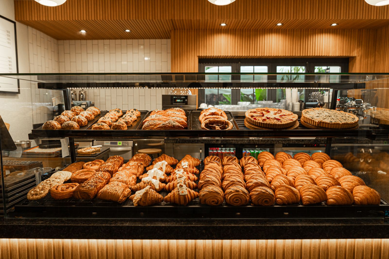 A bakery counter lit from above with trays of fresh pastries and buns