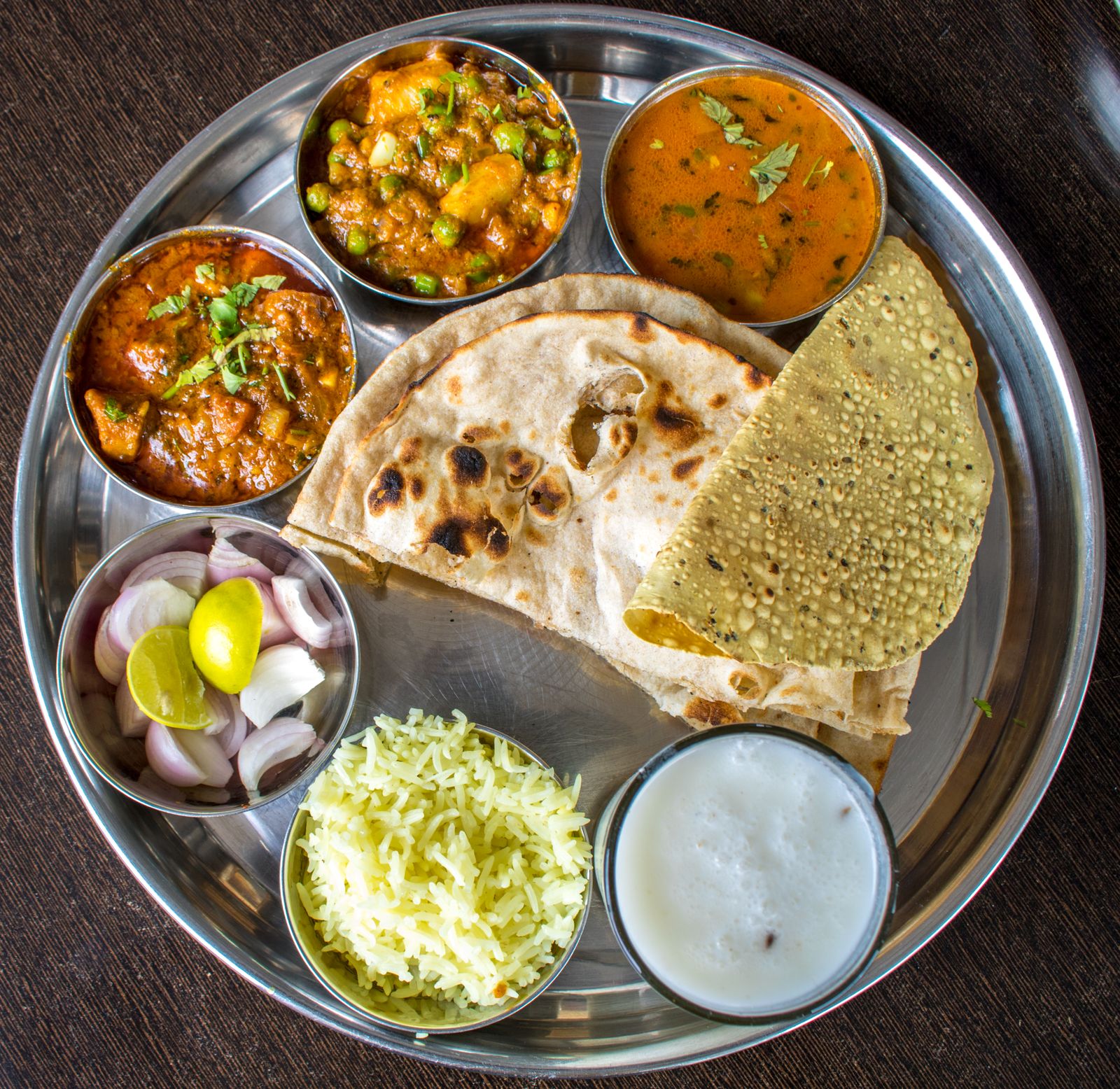 A steel thali plate with curries, rice, flatbread, salad and yogurt