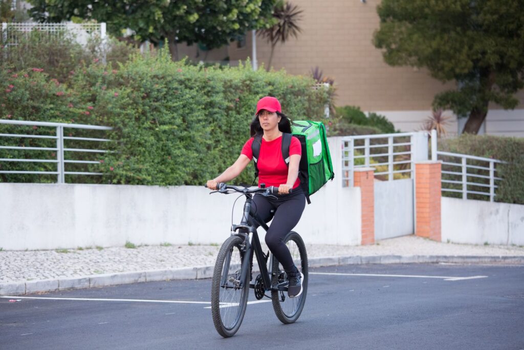 A rider with a green delivery backpack cycling through a quiet neighbourhood