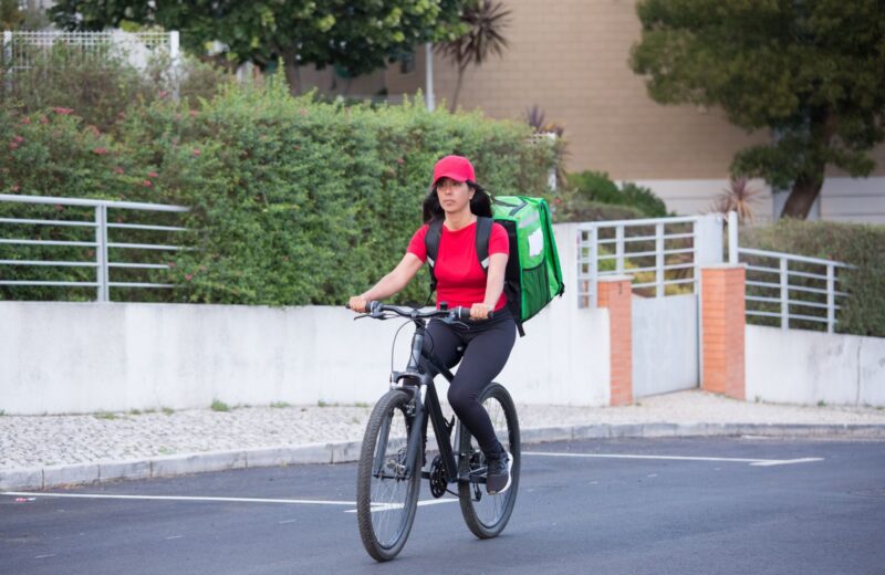 A rider with a green delivery backpack cycling through a quiet neighbourhood