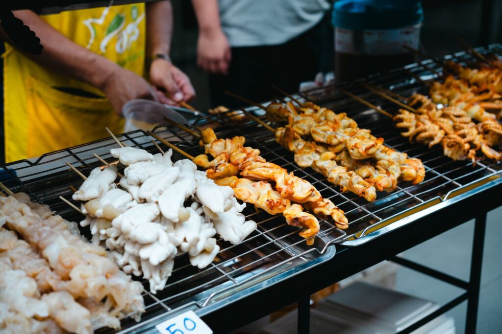 Skewers of meat and vegetables grilling side by side at a street food stand