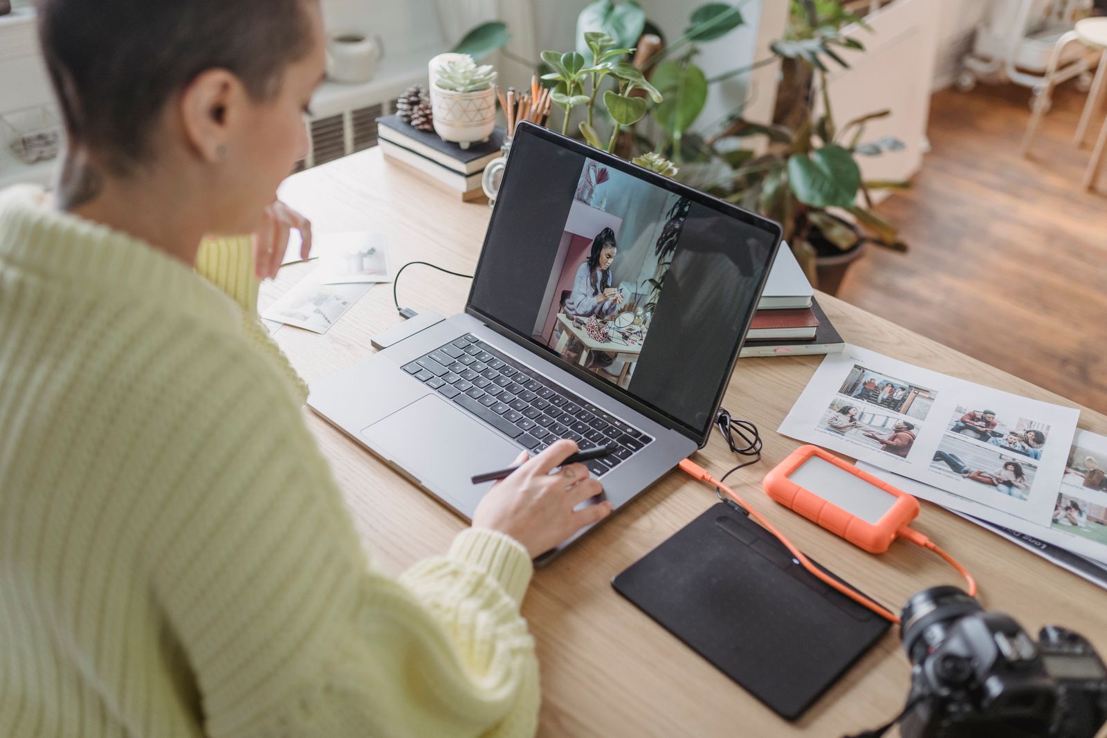 A photographer retouching a portrait on a laptop with a pen tablet and prints on the desk