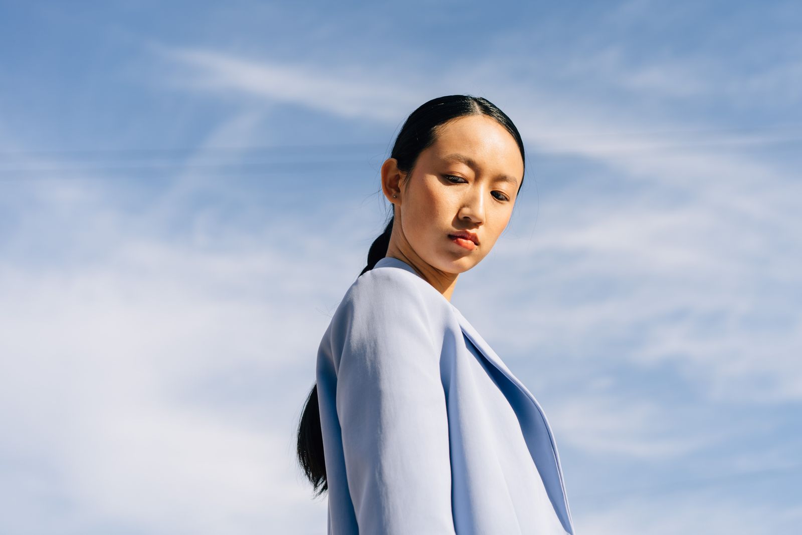A woman in a blue jacket photographed from below against a pale blue sky
