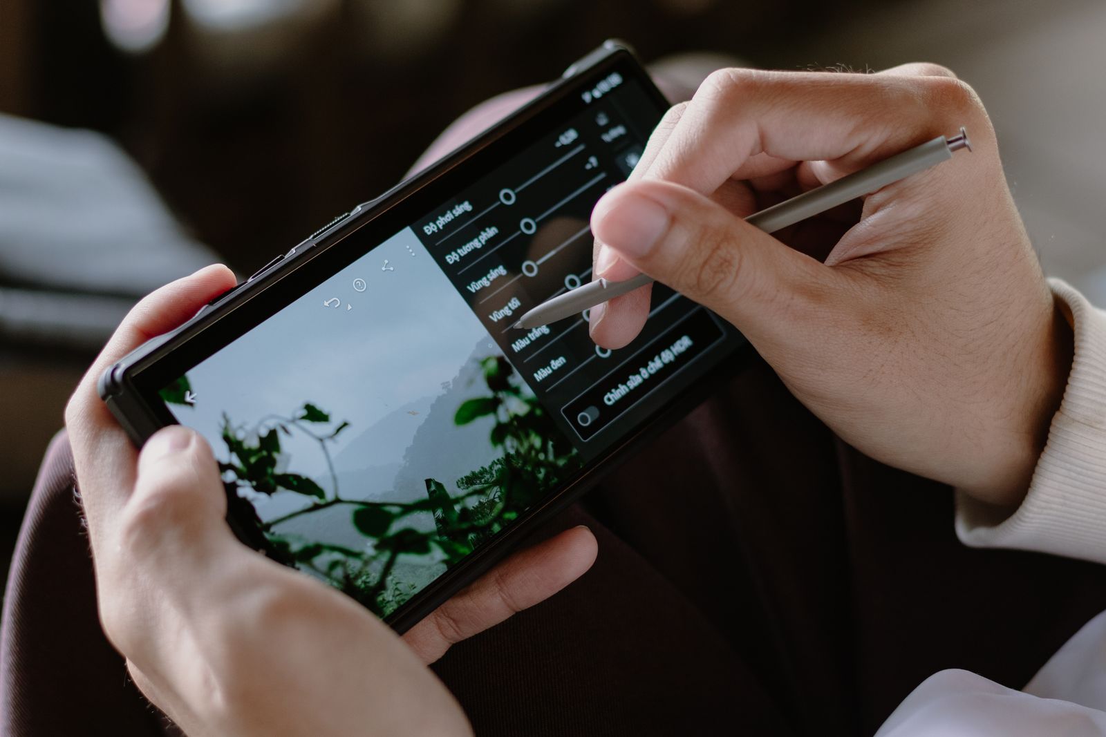 Hands holding a phone with a stylus, moving the light sliders on a misty hillside photo