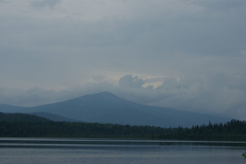 A mountain lake under a low grey sky, with dark forest on the far shore
