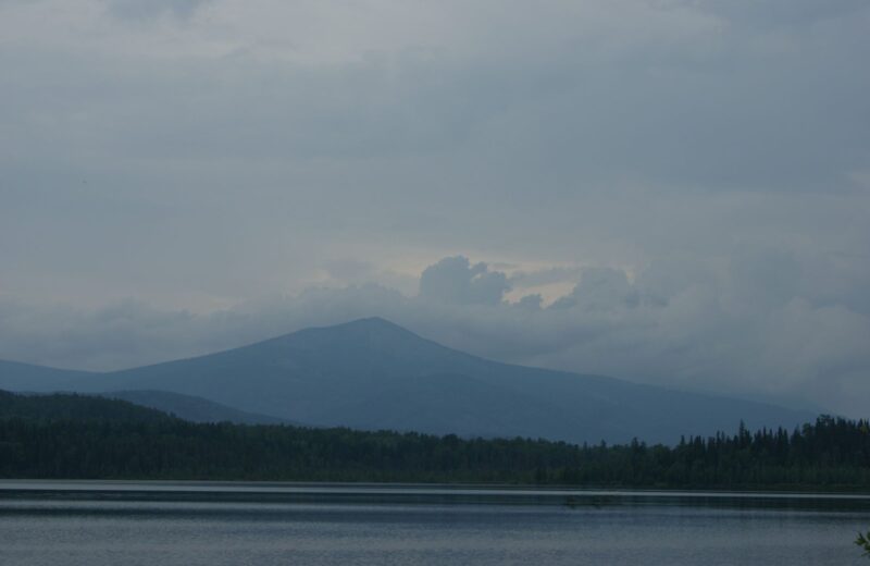 A mountain lake under a low grey sky, with dark forest on the far shore