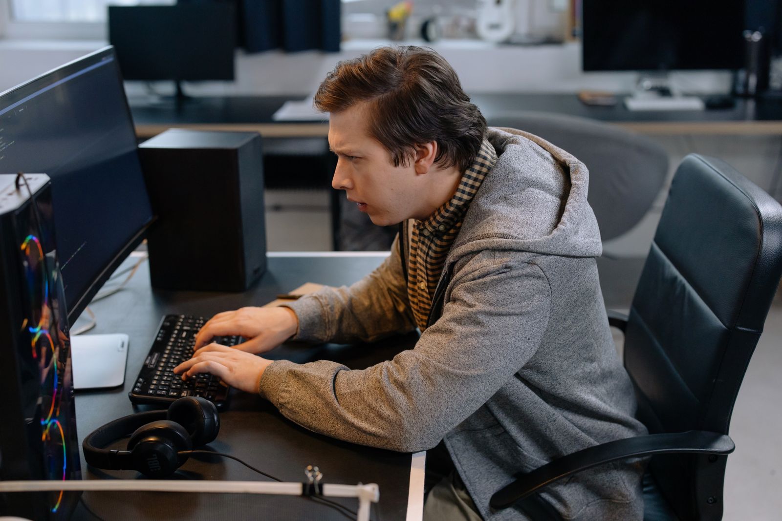 A developer in a grey hoodie typing at a desk in a studio office