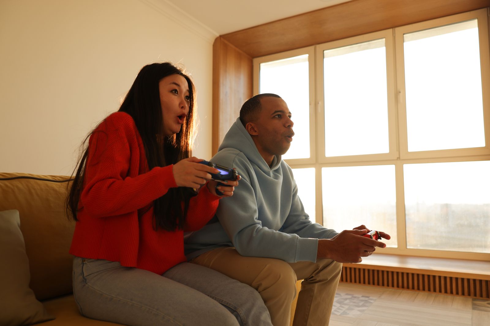 Two friends on a sofa by a big window, playing a game together