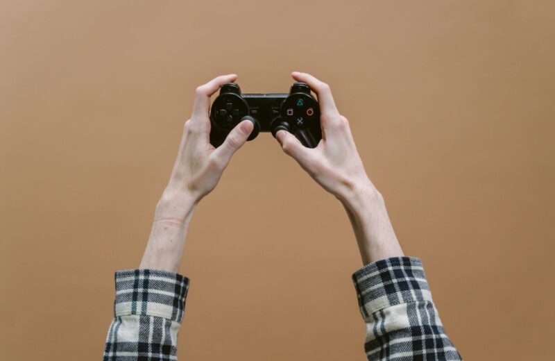 Two hands raising a gamepad against a plain brown wall