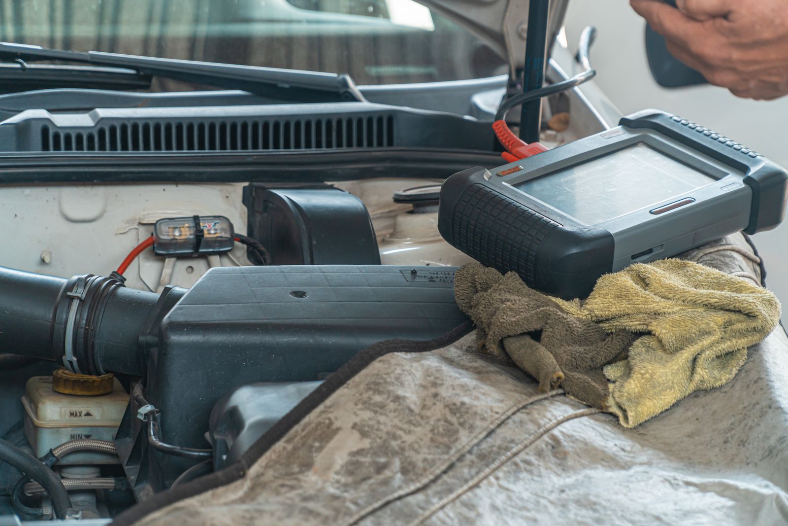 A diagnostic code reader resting on a wing cover next to an open engine bay