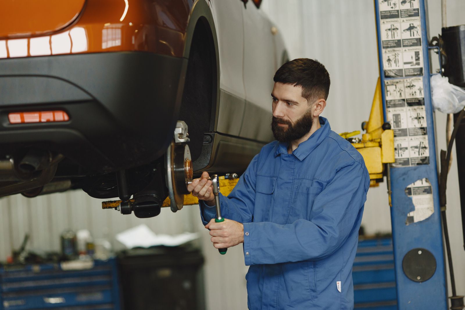 A mechanic working on a front wheel hub of a raised car