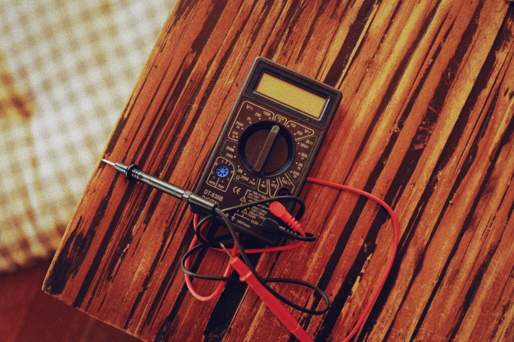 A digital multimeter with red and black test leads on a wooden bench