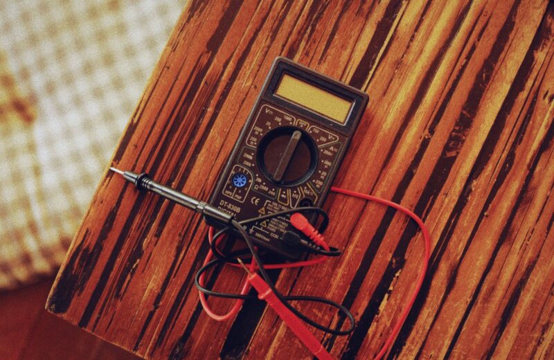 A digital multimeter with red and black test leads on a wooden bench