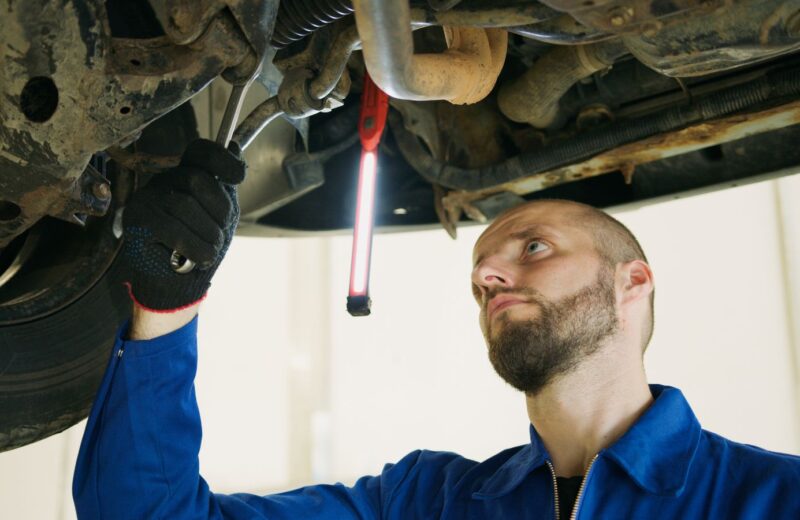 A mechanic checking the underside of a car with an inspection lamp
