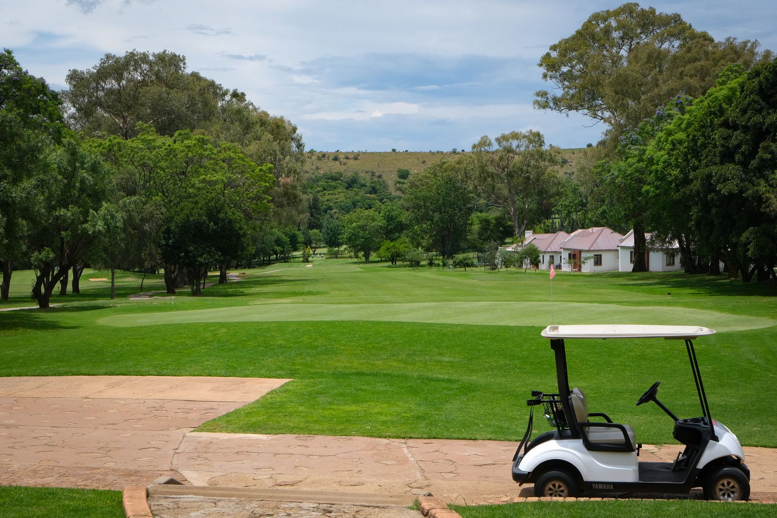 A golf buggy parked on the path beside a fairway, the clubhouse in the distance