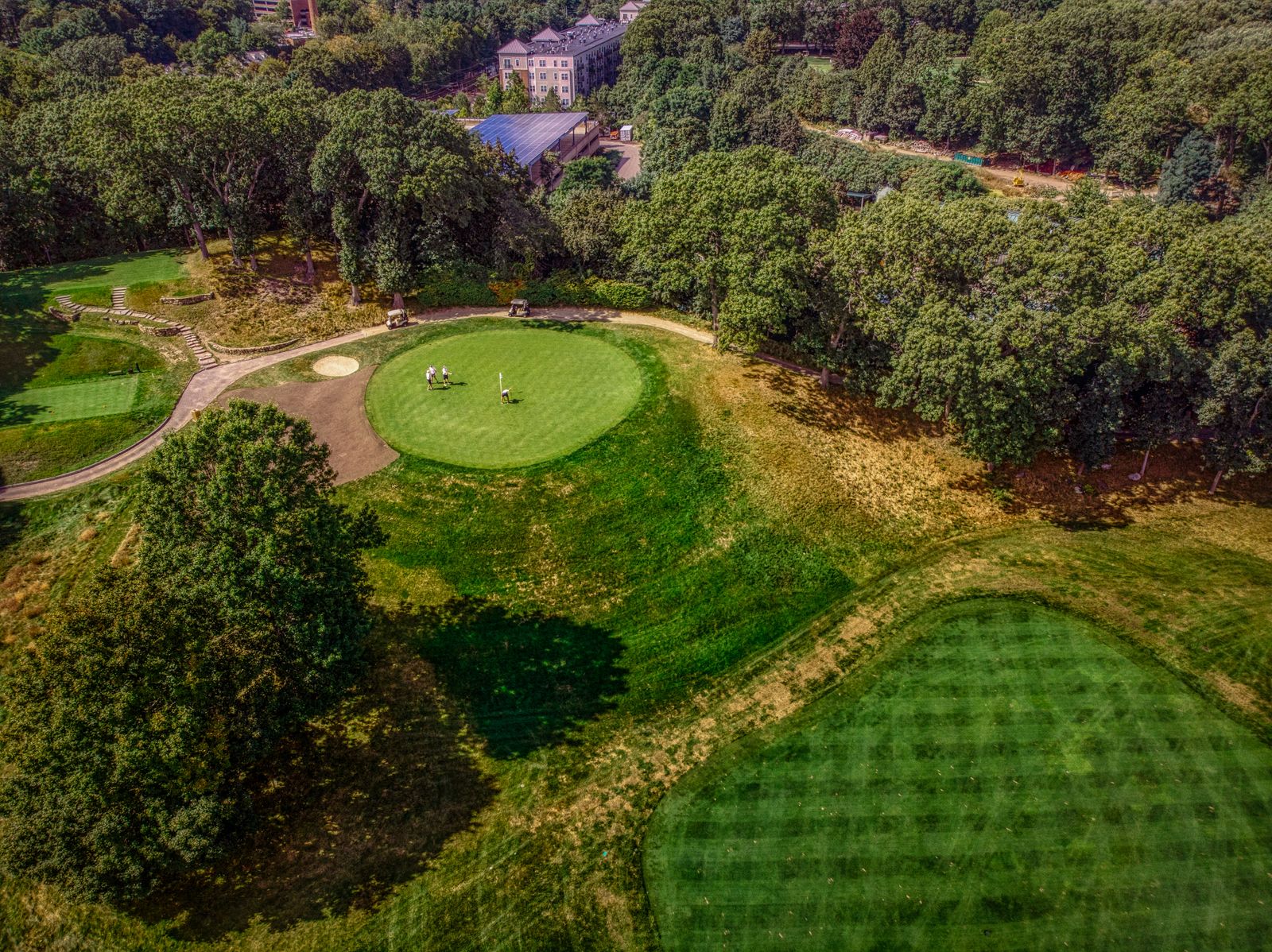 Aerial view of a parkland golf course: a green with bunkers among trees and striped fairways