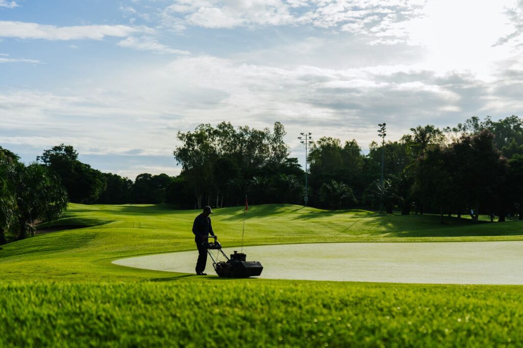 A greenkeeper mowing a green with a walk-behind mower