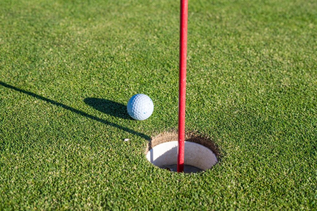 A golf ball resting at the edge of the hole beside a red flagstick