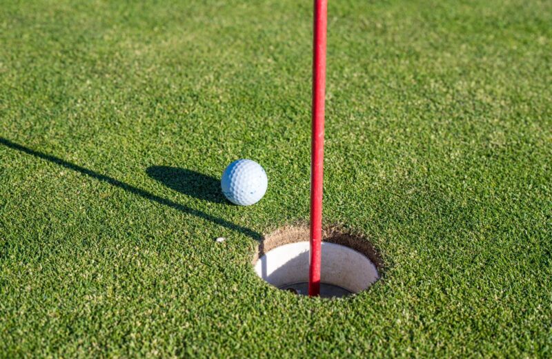 A golf ball resting at the edge of the hole beside a red flagstick