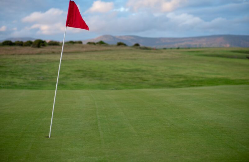 A red flag on a green under a clear blue sky