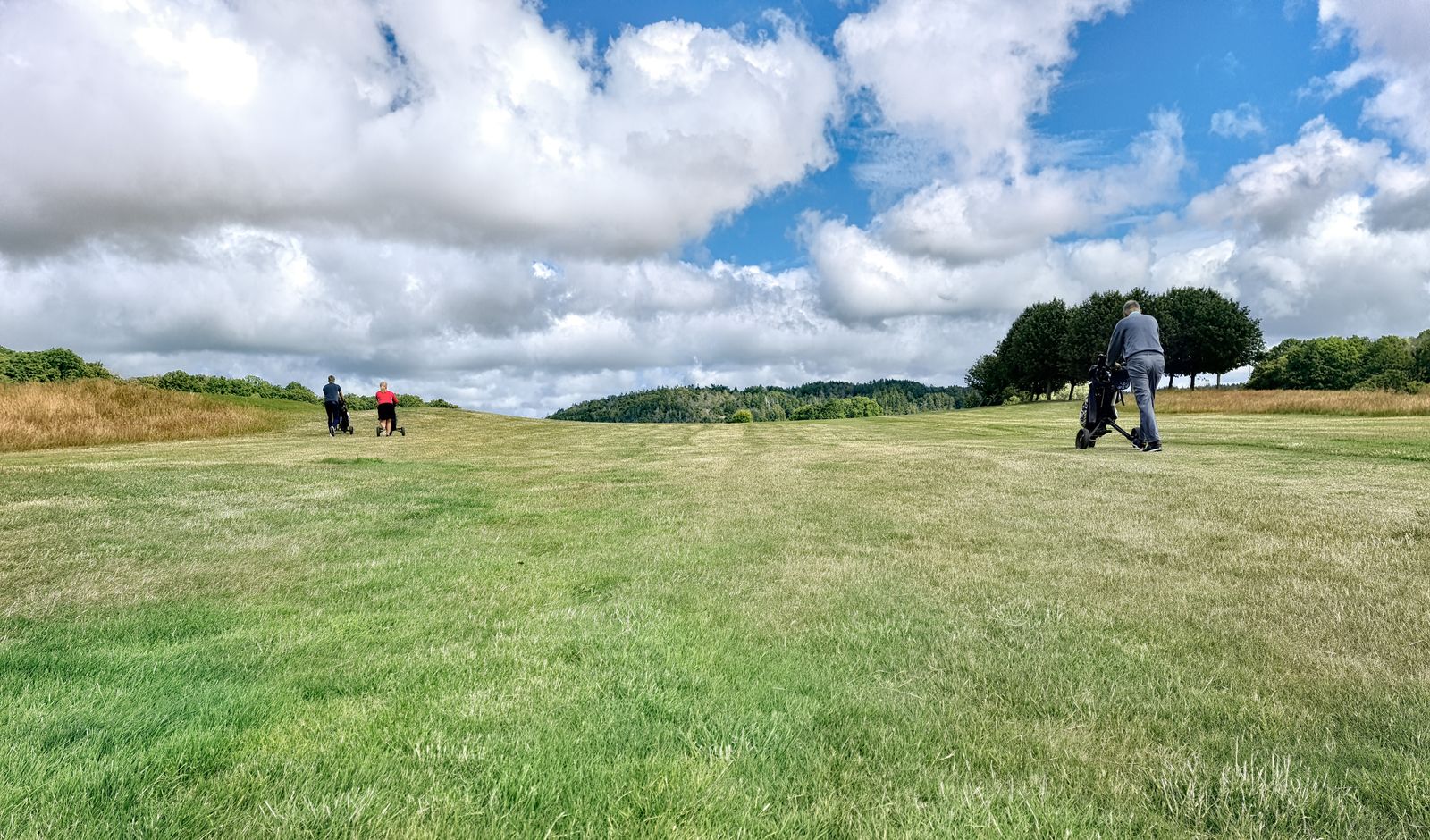 Two golfers walking a fairway with their trolleys under a wide cloudy sky
