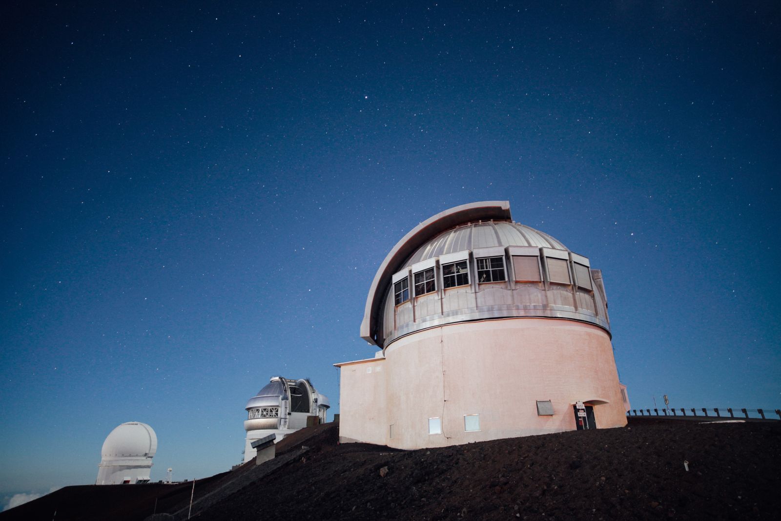 A white observatory dome with its shutter closed on a dark hilltop under a starry sky