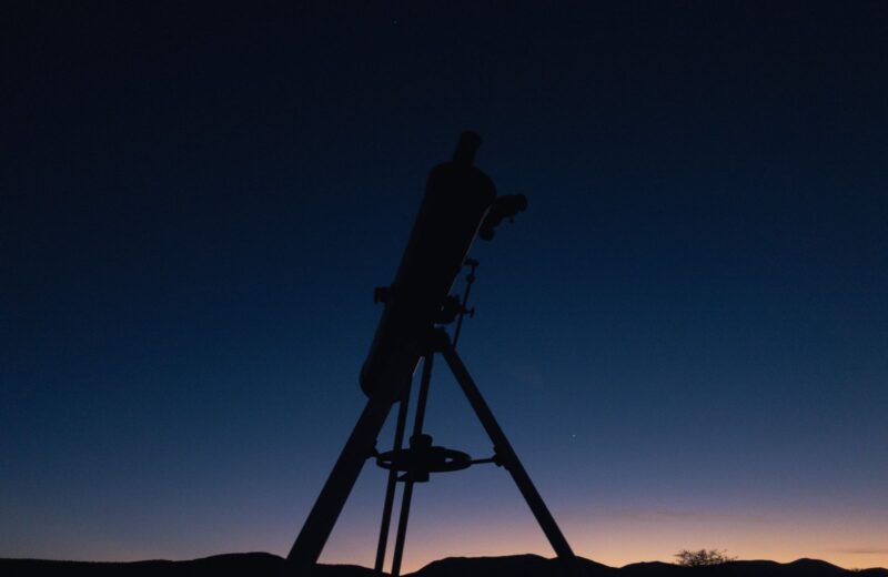 A telescope on a tripod in silhouette against a blue twilight sky
