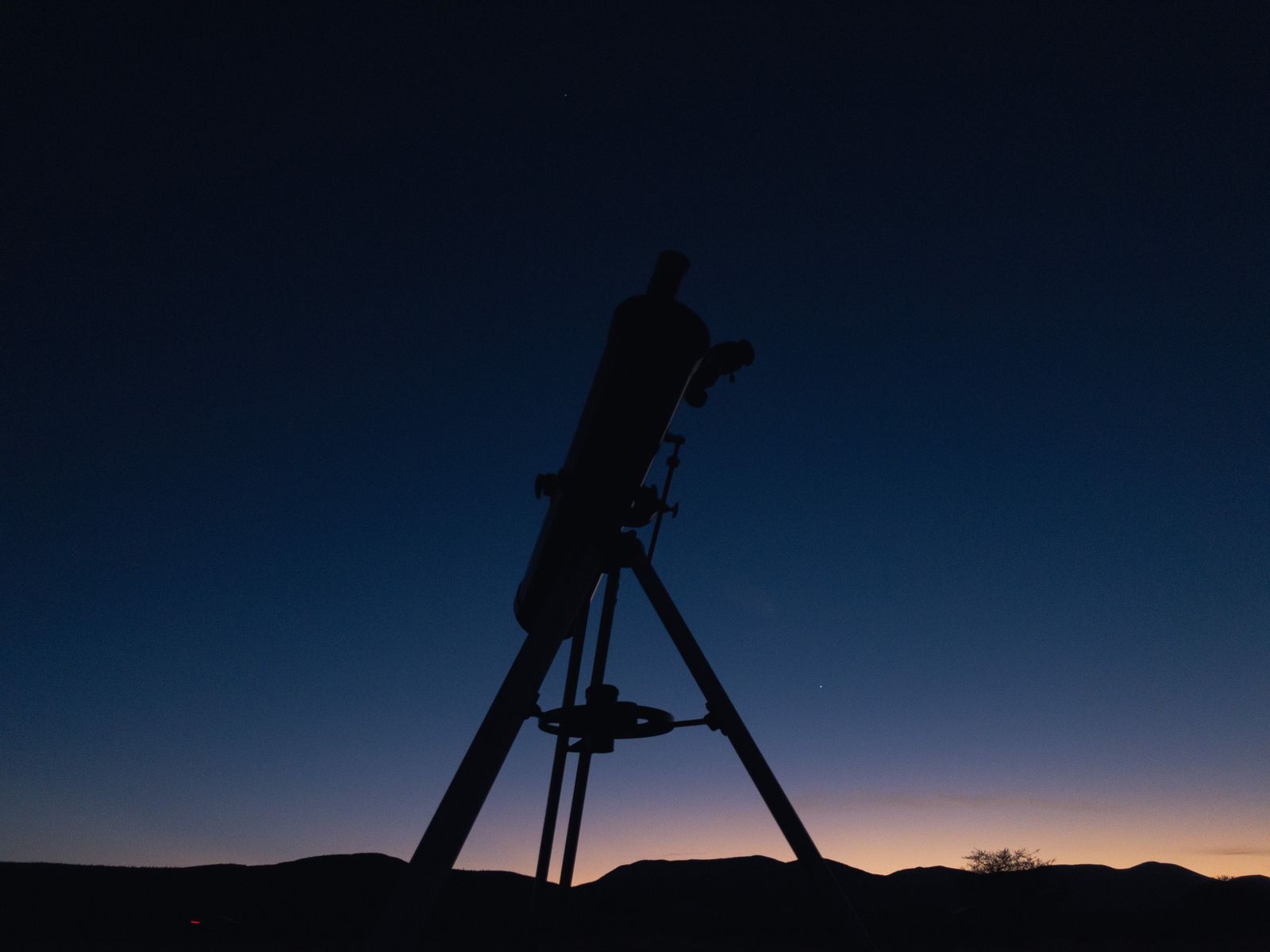 A telescope on a tripod in silhouette against a blue twilight sky