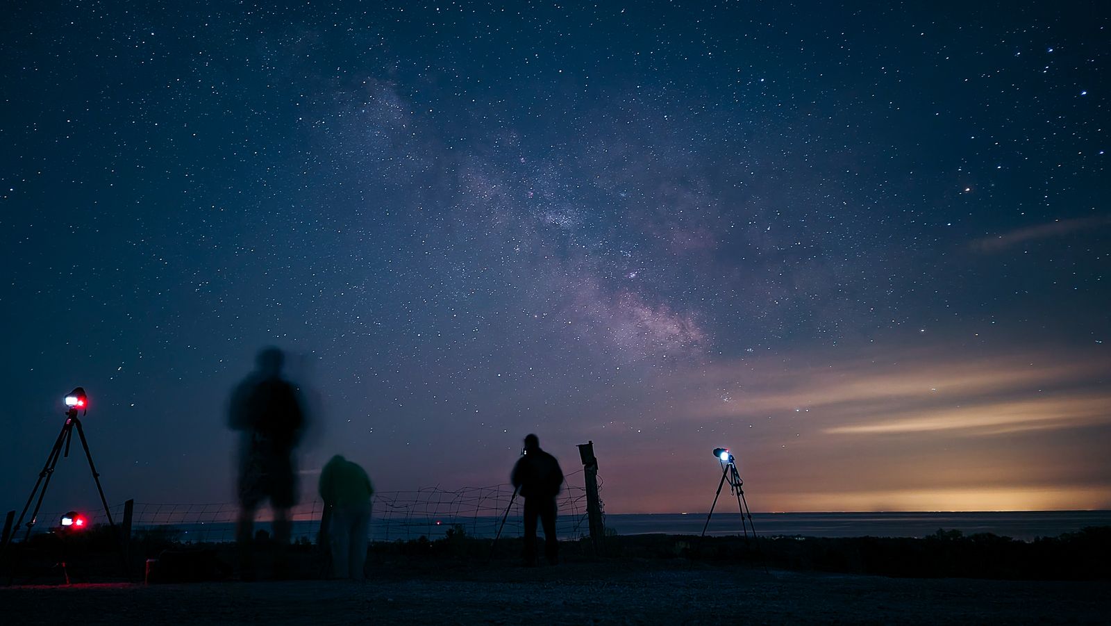 A few people with a telescope under the Milky Way on open ground at night