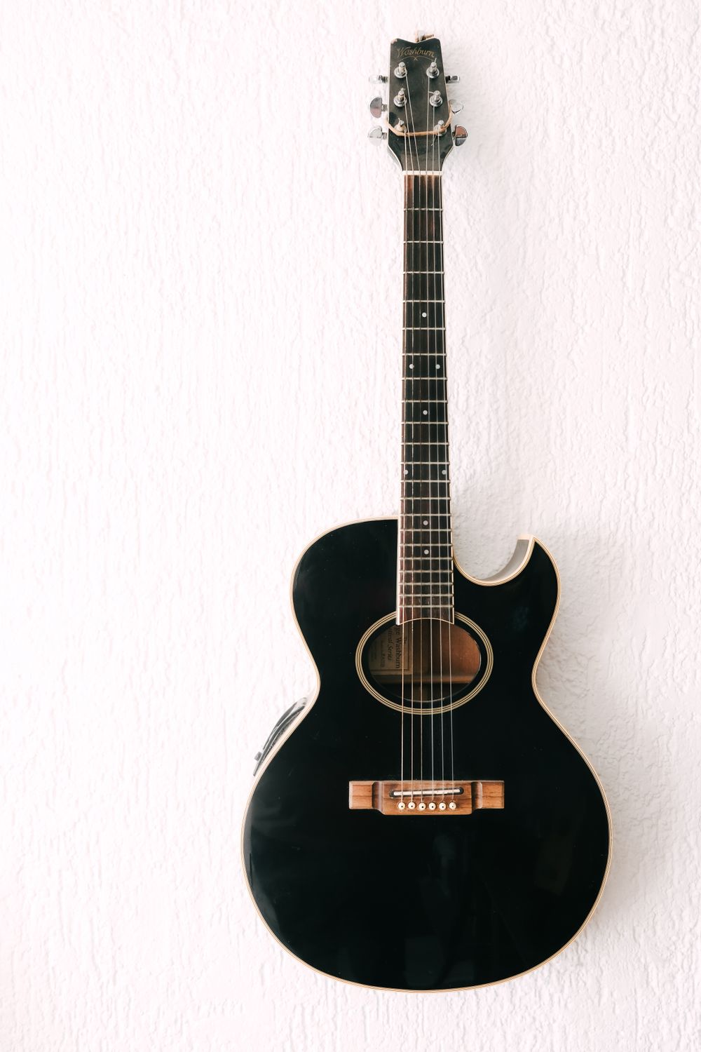 A black cutaway acoustic guitar leaning against a white wall