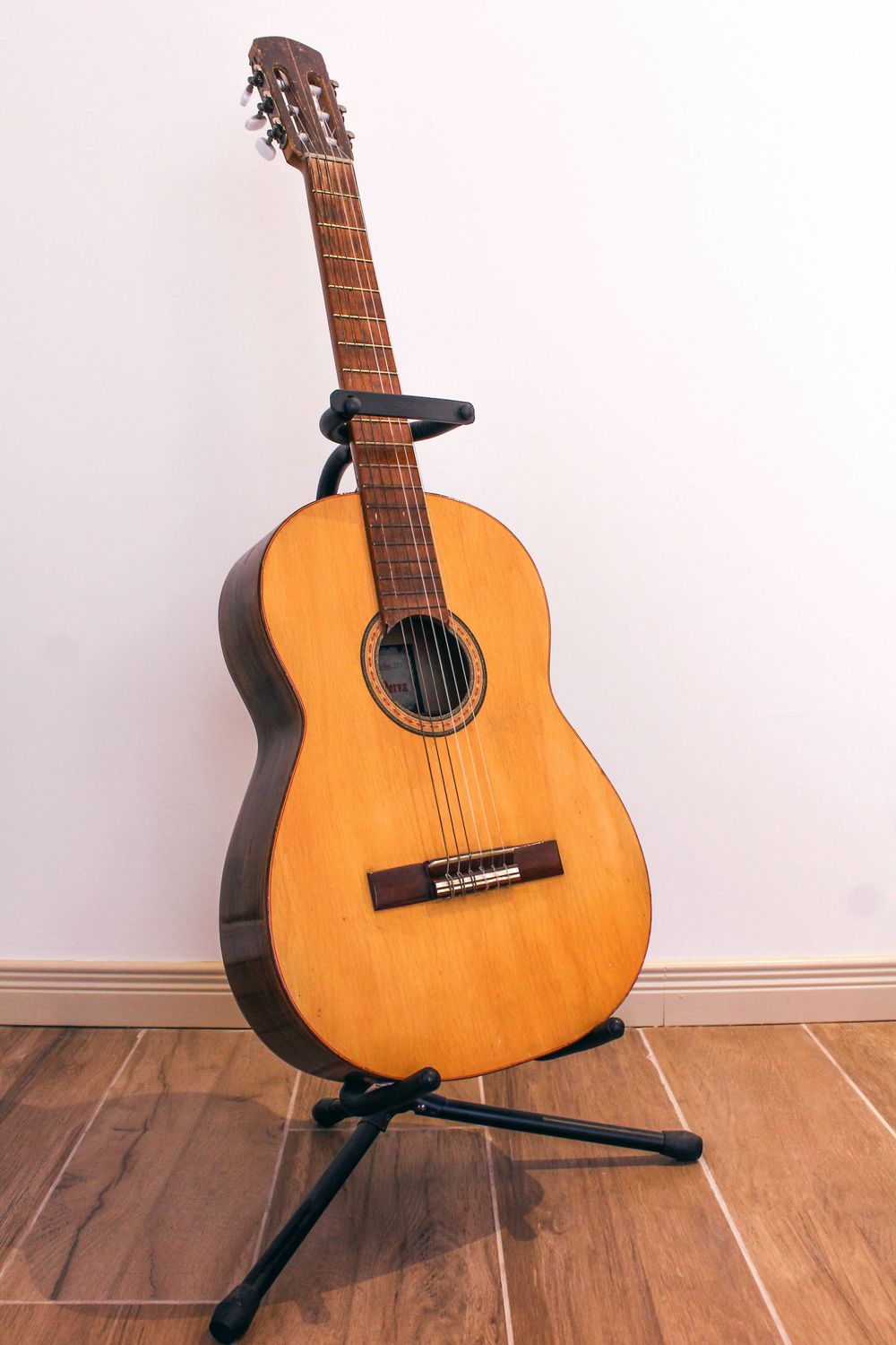 A classical guitar with a natural spruce top on a stand against a white wall